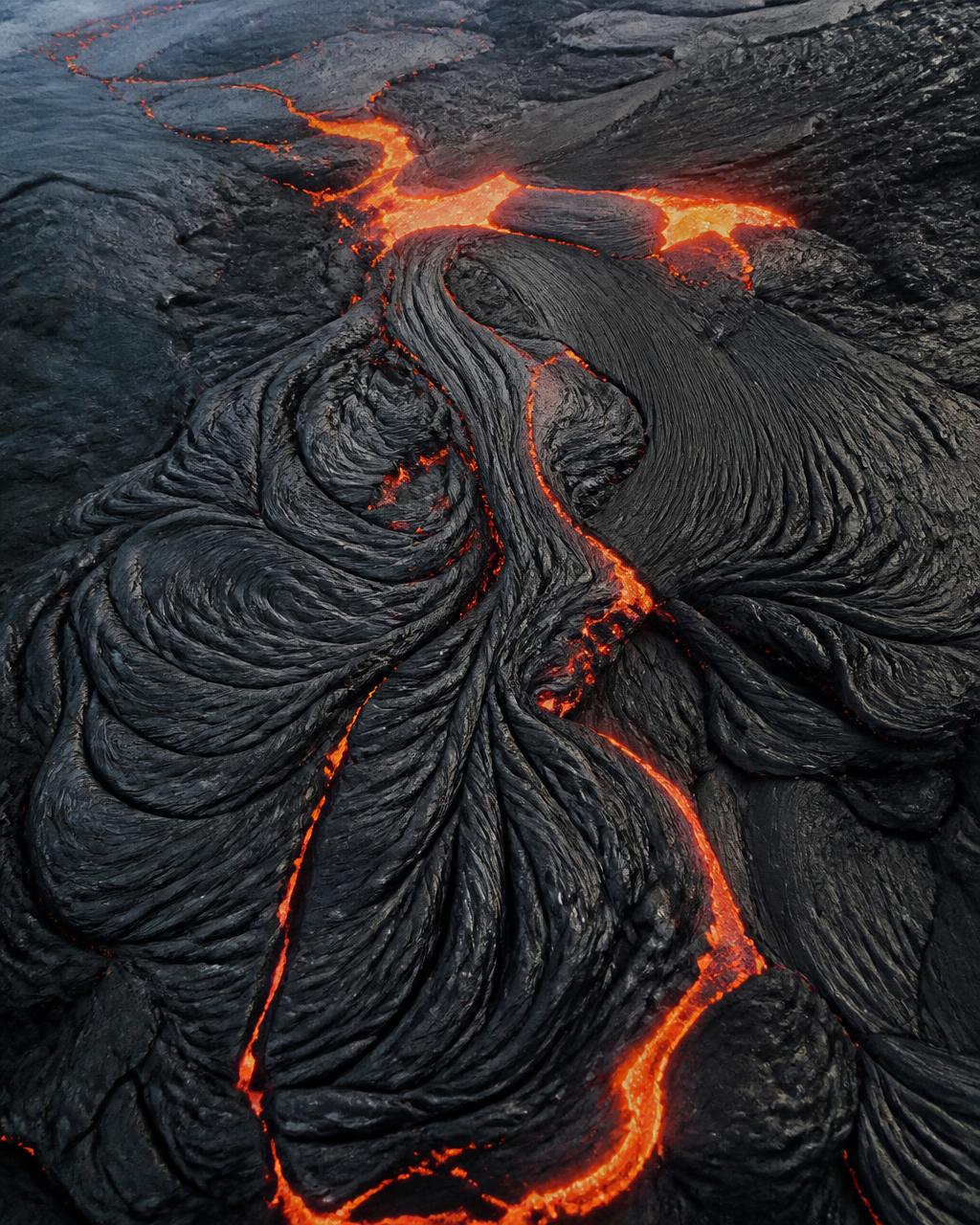 Aerial view of cooling black pahoehoe lava with glowing orange cracks in the folds