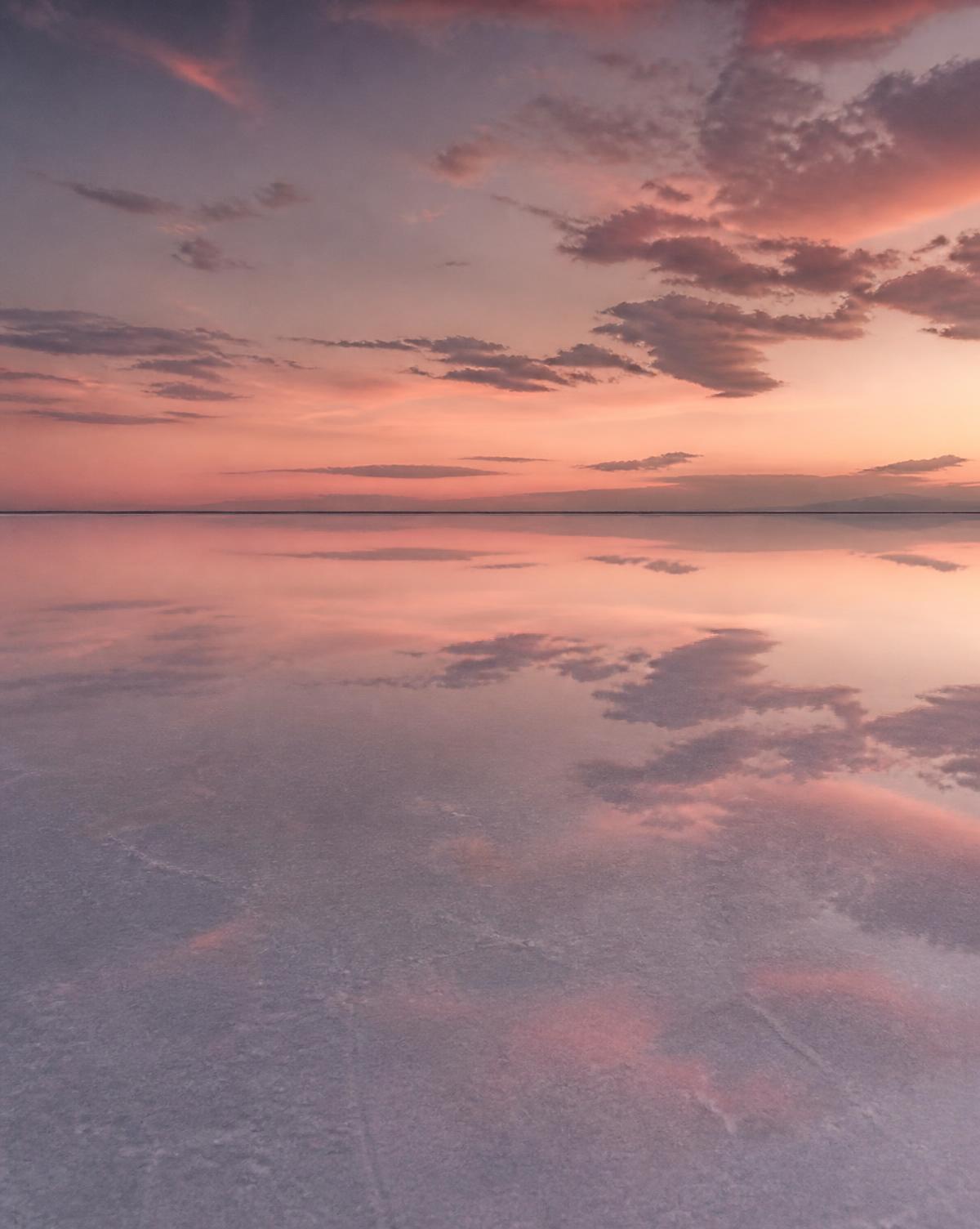 Salt flat covered in a thin water film mirroring a pink and lilac dusk sky