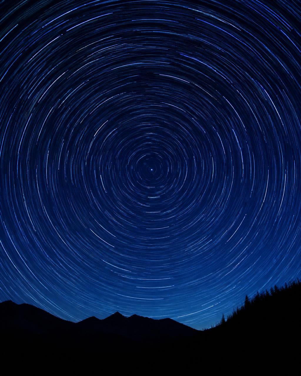 Long-exposure night sky with circular star trails around a central stationary star